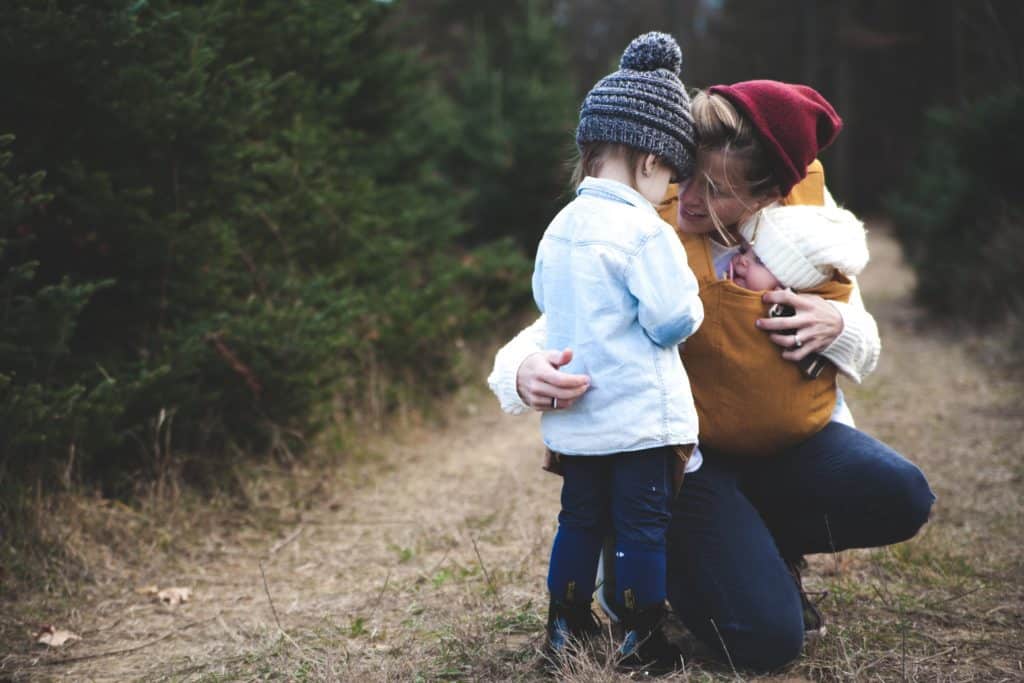 Ein (Bonus)Mutter kümmert sich um ihr Stiefkind mit ihrem leiblichen Kind in der Trage