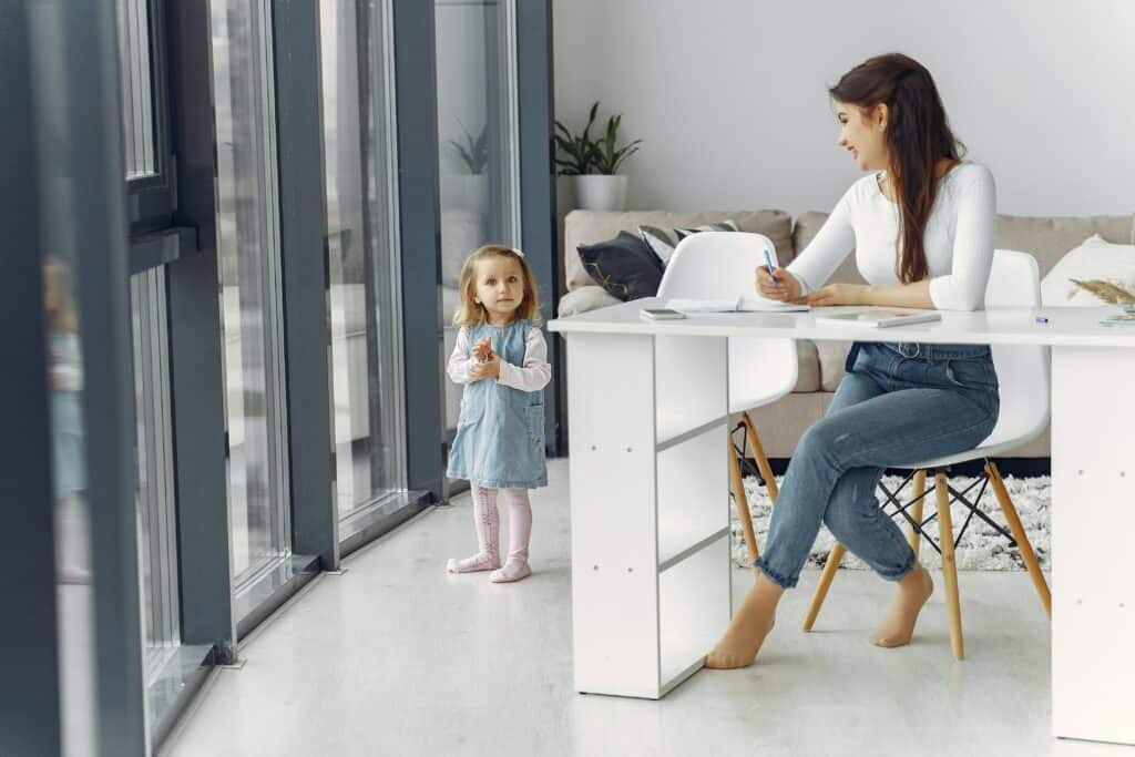 Heldenreise als Stiefmutter: Frau sitzt am Schreibtisch und arbeitet, neben ihr steht ein kleines Mädchen.