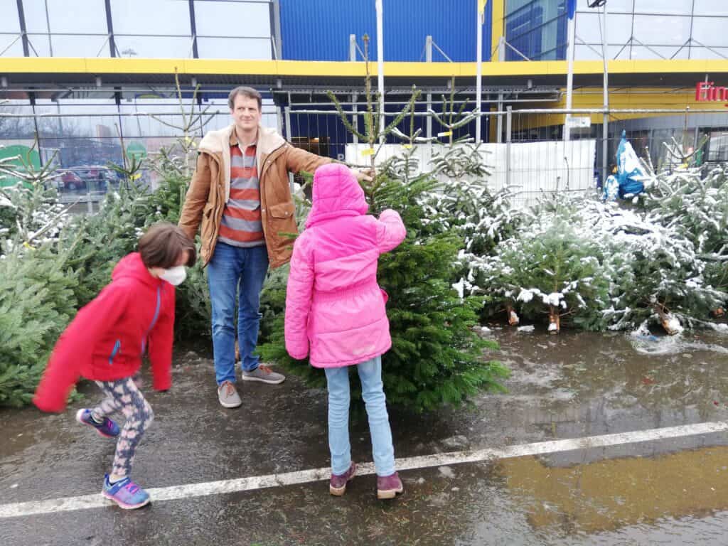 Tannenbaum kaufen ohne Bonuskind. Papa hält den Baum, die Mädchen diskutieren.