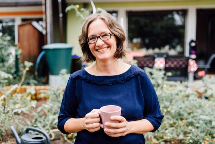 Marita steht mit einem Kaffee in der Hand im Garten. Einladung zum Perspektivwechel, um die Trennung zu verstehen.