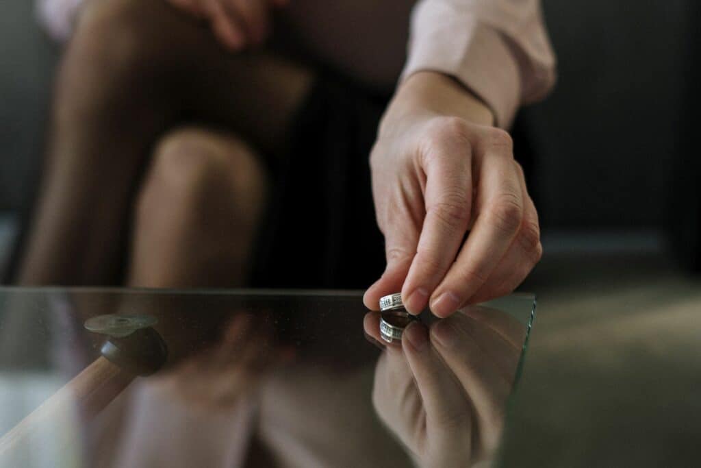 Frau legt einen Ehering auf einem Glastisch ab. Trennung braucht sichtbare Zeichen. 